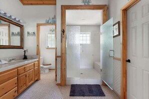 A bathroom with a wooden vanity, a toilet, a glass shower enclosure, and a door leading to another room. - Waterview Lodge. New Addition. Spa. Lake views. (Big Bear Lake)