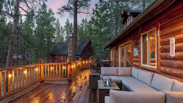 A wooden deck with a sofa and a table, surrounded by trees. - Waterview Lodge. New Addition. Spa. Lake views. (Big Bear Lake)