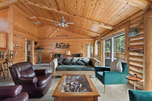 A log cabin interior with a wooden ceiling, a sofa, a leather armchair, and a coffee table.