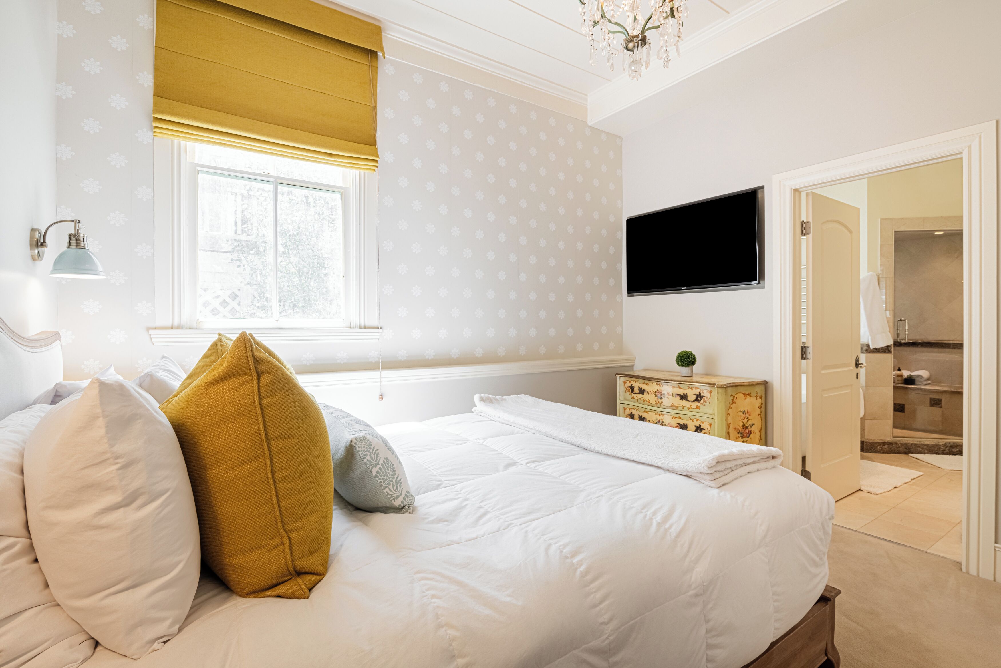 Ein Schlafzimmer mit einem Bett, einem Fenster mit Jalousien, einem an der Wand befestigten Fernseher und einer Kommode.