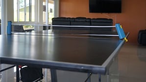 A ping pong table in a room with a TV on the wall and a couch in the background. - Private Retreat Getaway (Florence Hall Village)