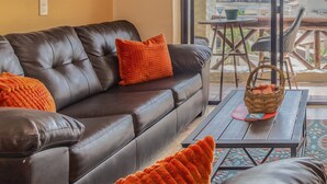 Ein modernes Wohnzimmer mit einem Ledersofa, orangefarbenen Zierkissen und einem Korbwäscheskorb auf einem Holztisch.