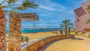Blick auf einen Strand mit einem Steinweg, Palmen und blauem Himmel.