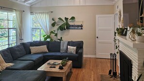A living room with a sectional sofa, a coffee table, a fireplace, and a large window with curtains.