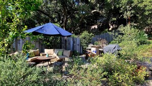 A backyard with a wooden fence, a blue umbrella, outdoor furniture, and various plants.