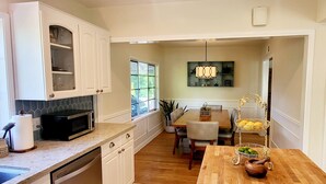 A kitchen with a microwave, sink, and cabinets. There is a dining table with chairs and a hanging light fixture.