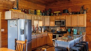 A rustic kitchen with wooden cabinets, a stainless steel refrigerator, a microwave, and a coffee maker. - Teal Door Escape- country living close to town (Cody)