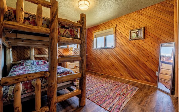 Interno rustico di una baita con un letto a castello in legno, una finestra con vista e pavimento in legno.
