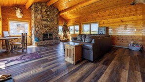 A log cabin interior with a stone fireplace, leather sofa, and a stone wall. - Teal Door Escape- country living close to town (Cody)
