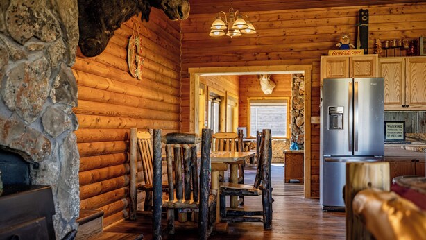 A rustic cabin interior with a stone fireplace, wooden dining table, and a refrigerator. - Teal Door Escape- country living close to town (Cody)