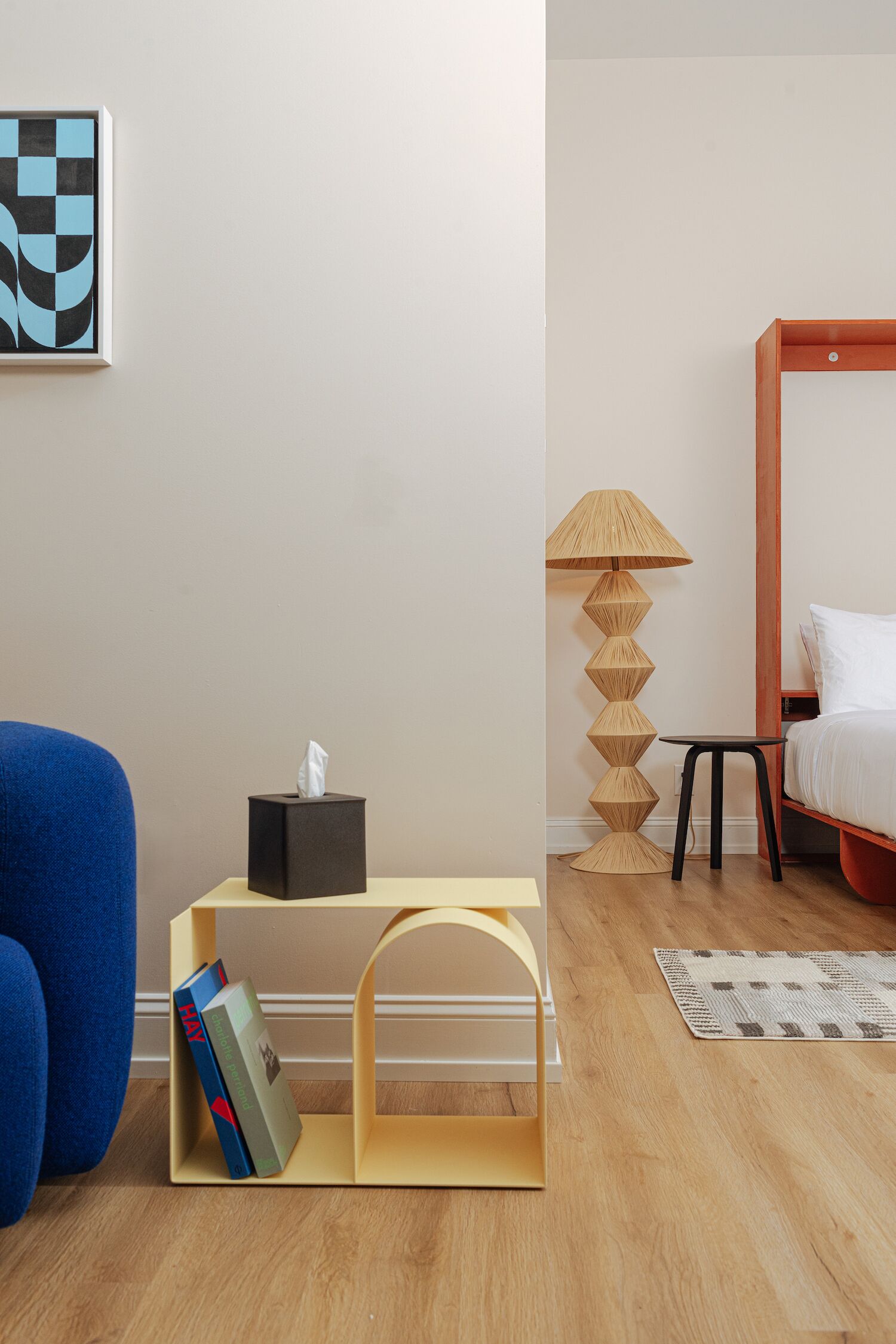 A modern bedroom with a bed, bedside table, lamp, and a blue chair.