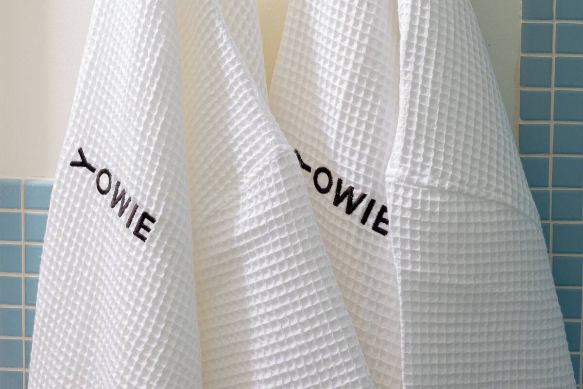 Two white towels hanging on a wall-mounted towel rack with the name "OWIE" embroidered on them.