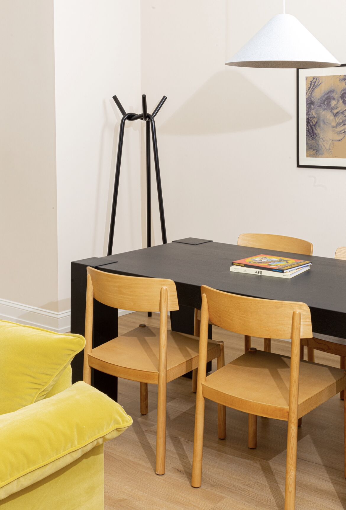 A dining area with a black table, wooden chairs, a yellow sofa, and a floor lamp.