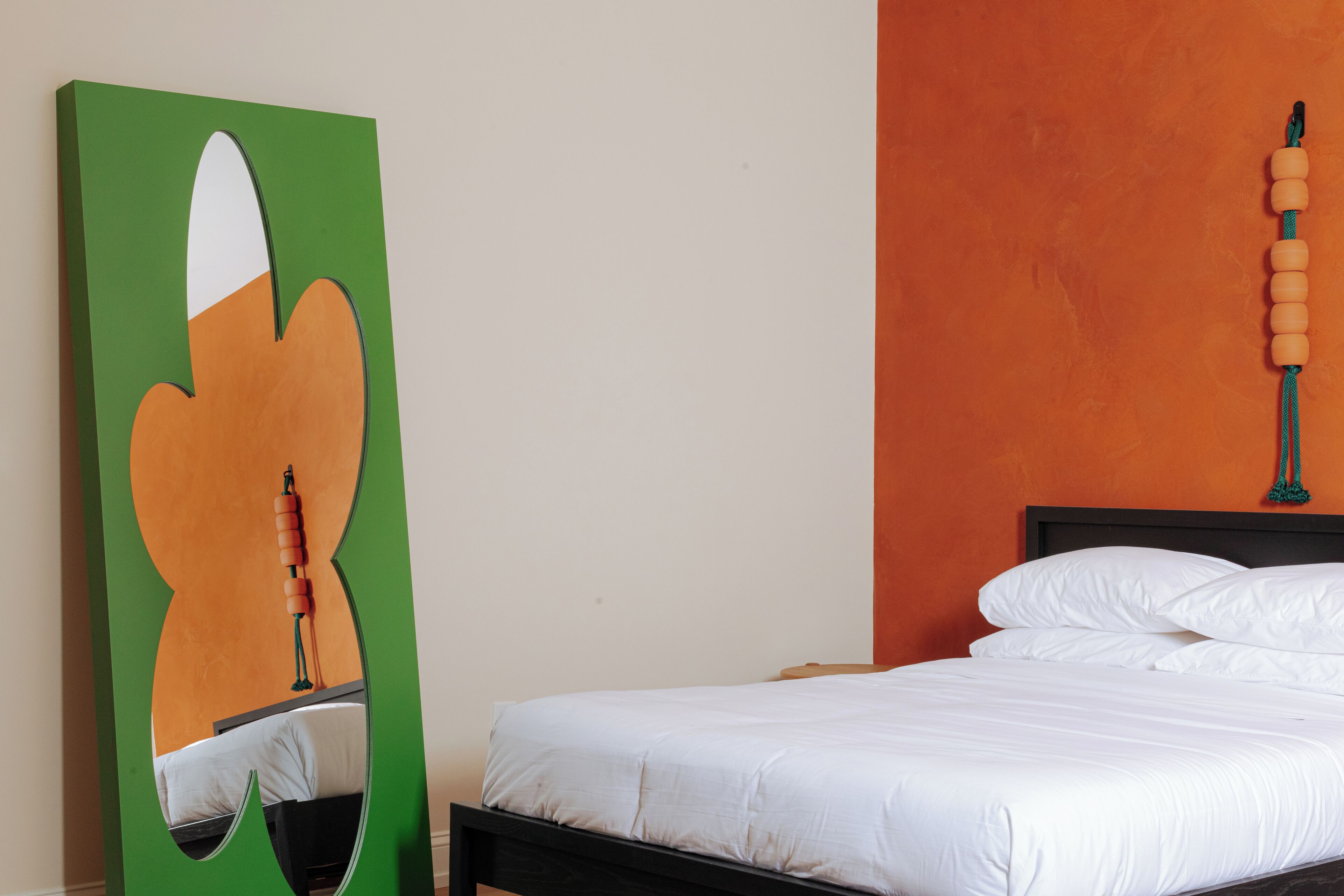 A neatly made bed with white linens, a green abstract artwork on the wall, and a wooden headboard.