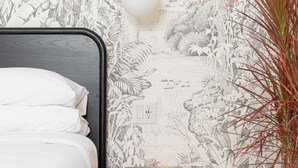 A bedroom with a bed, a wall mural, a hanging light, a small orange storage unit, and a potted plant. - YOWIE (Hotel & Shop) (Philadelphia)