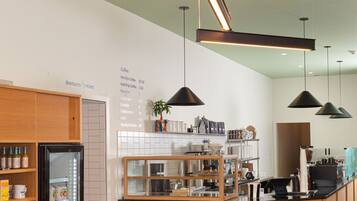 L’intérieur d’un café moderne présente un comptoir en bois, une vitrine réfrigérée et un tableau affichant le menu au mur.