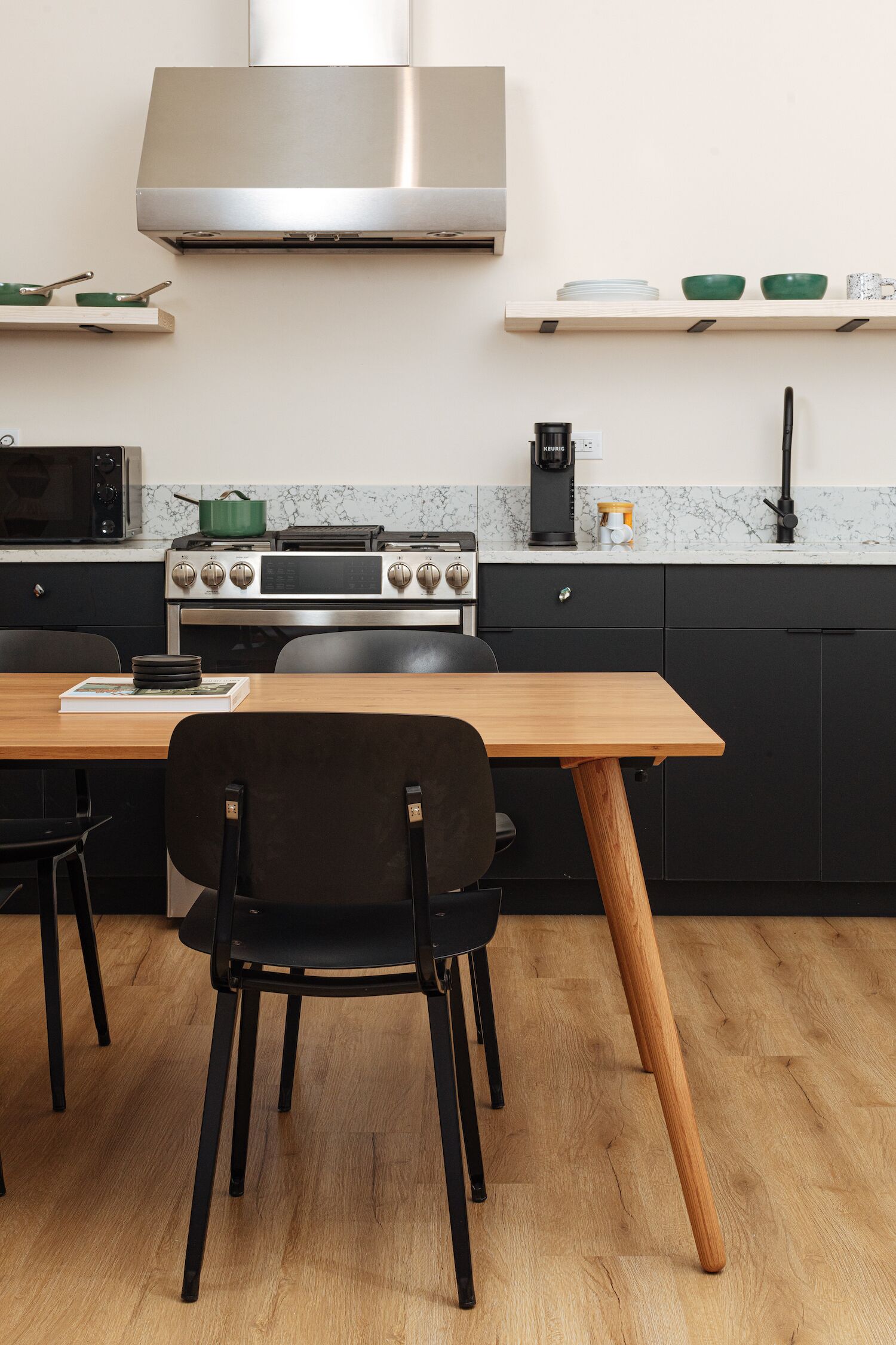 A modern kitchen with a wooden table, black chairs, a stove, and a microwave.