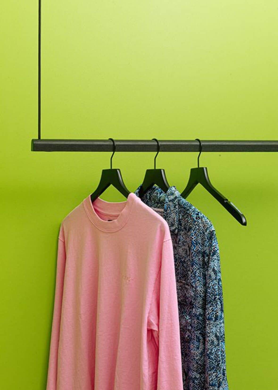 Arara de roupas com duas peças penduradas em frente a uma parede verde.