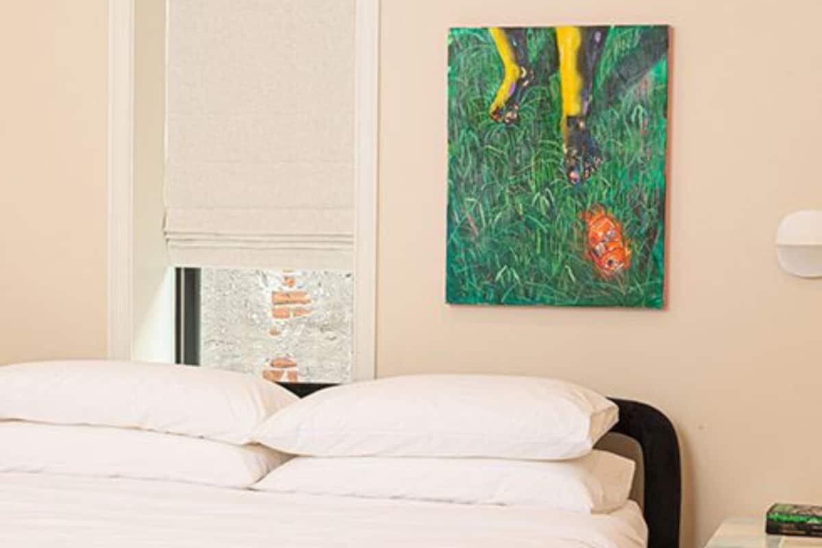 A bedroom with a bed, a painting, and a window with blinds.