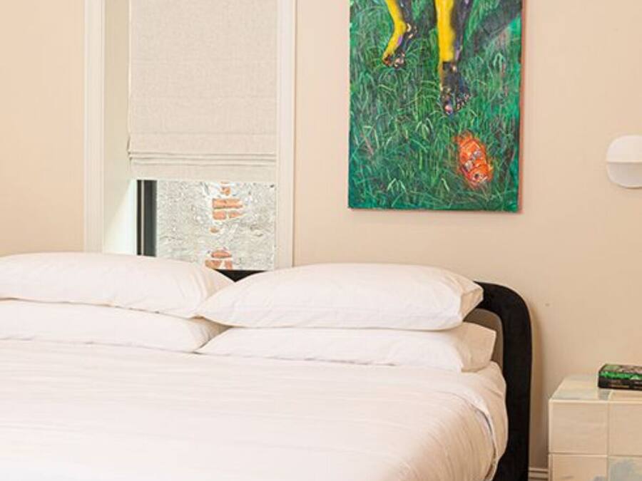 A bedroom with a bed, a painting, and a window with blinds.