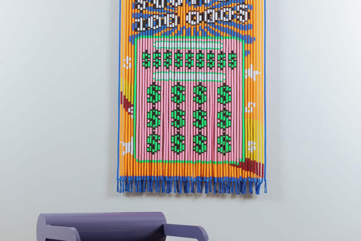 A room with a purple chair, a small round table with a blue mug, and a colorful tapestry on the wall.