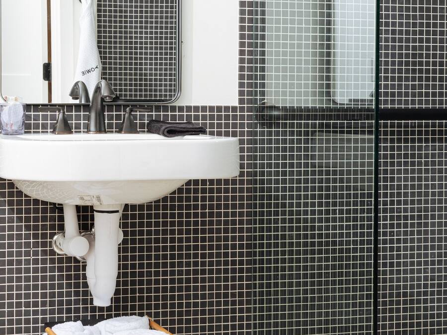 Ein Badezimmer mit einem weißen Waschbecken, einem Spiegel und einer gefliesten Wand.