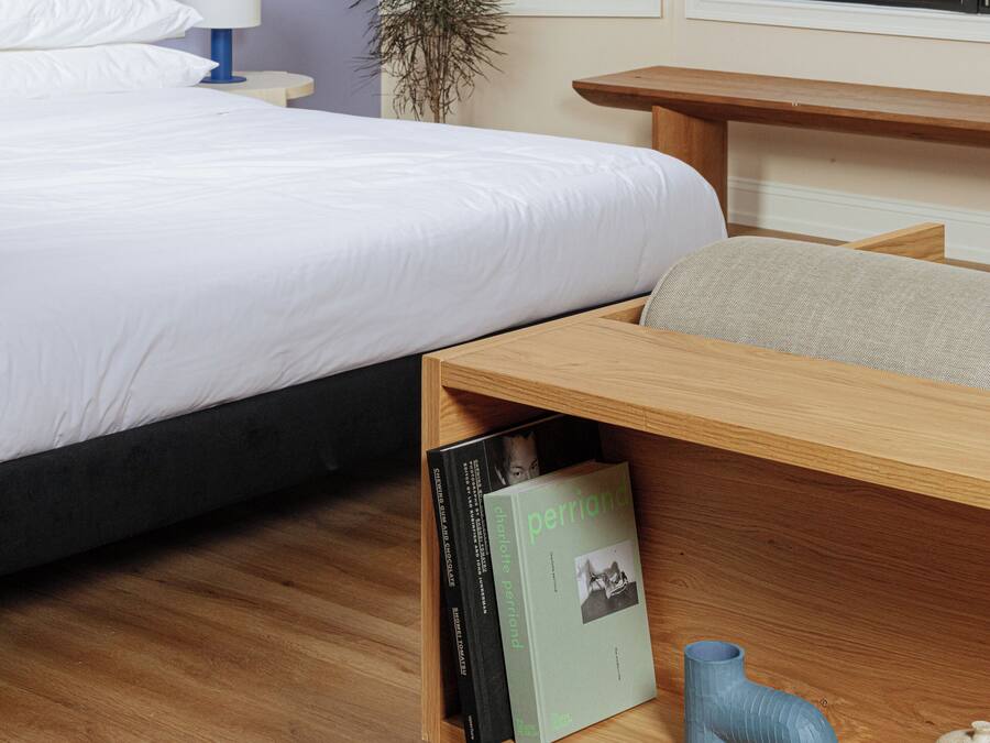 A bedroom with a bed, bedside table, lamp, and a shelf with books and decorative items.