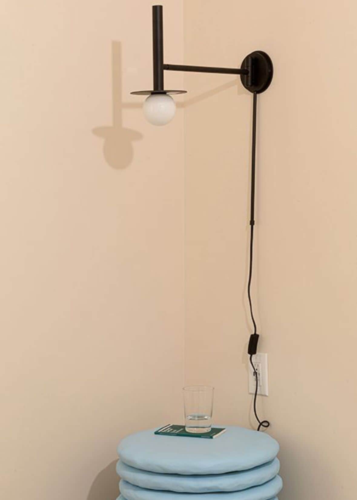A wall-mounted light fixture with a spherical bulb, a black cord, and a glass of water on a blue cushion.