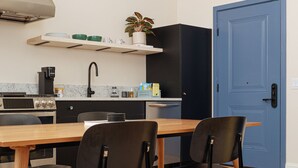 A modern kitchen with a wooden table and black chairs, a blue door, and a small plant on the shelf. - YOWIE (Hotel & Shop) (Philadelphia)