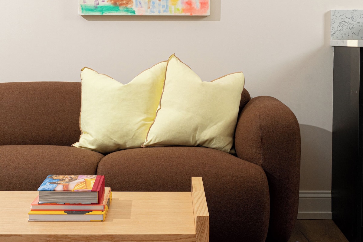 A brown sofa with two pillows, a wooden coffee table with books, and a purple rug with circular cutouts.