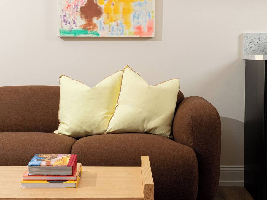 A brown sofa with two pillows, a wooden coffee table with books, and a purple rug with circular cutouts.