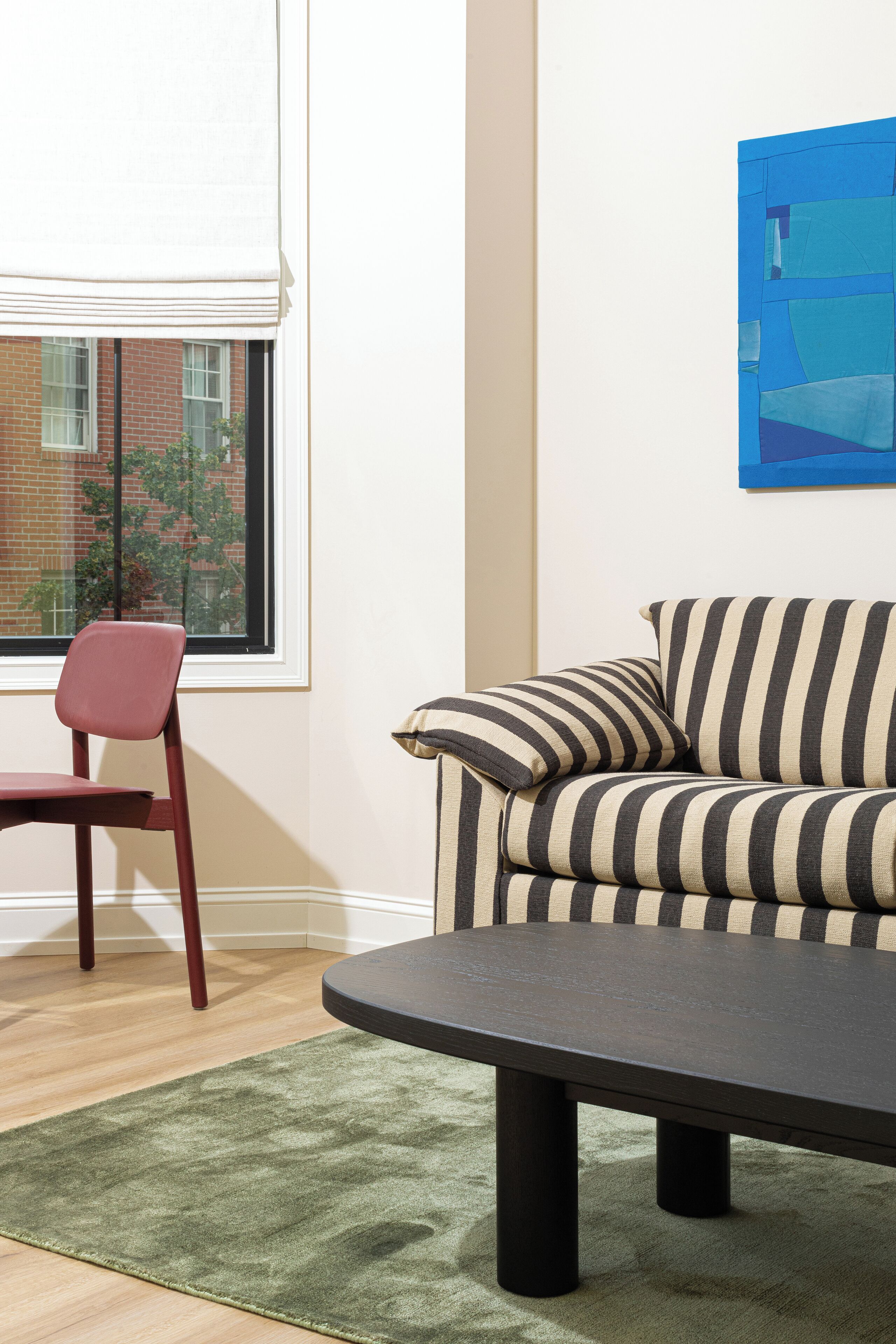 A room with a striped sofa, a red chair, a dark table, and a green rug.