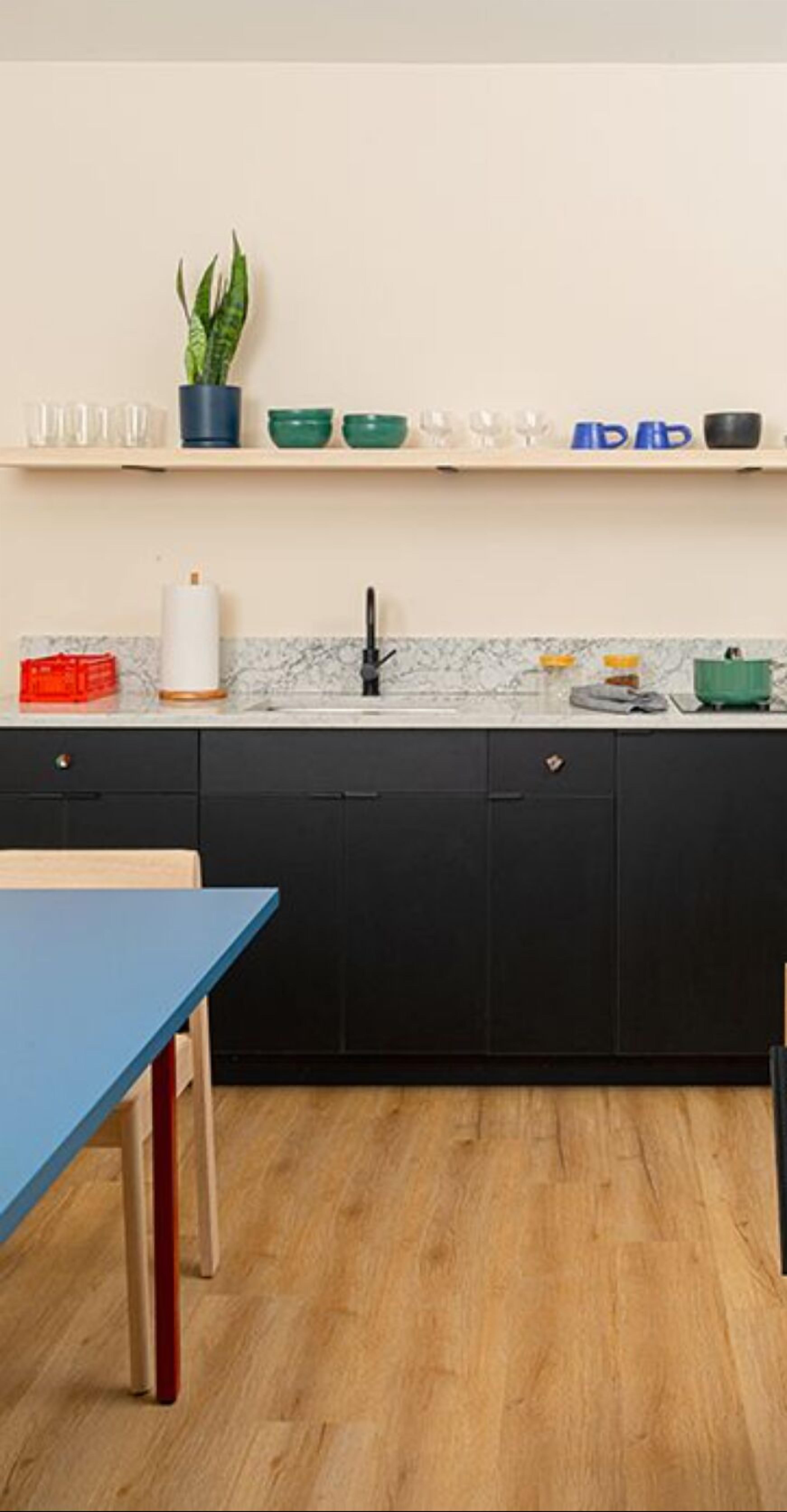 A modern kitchen with black cabinets, a marble backsplash, and a wooden floor.