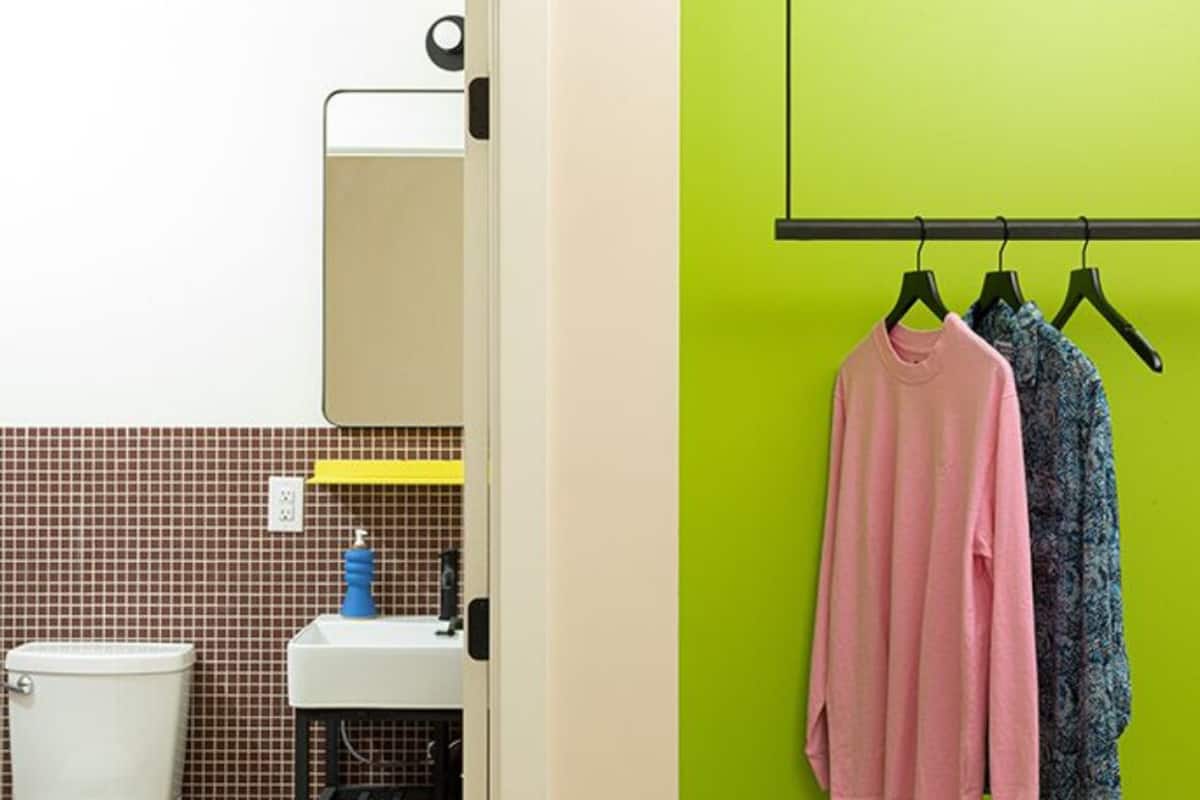 A bathroom with a white toilet, a sink, and a mirror. There is a green wall with a black rack holding two items.