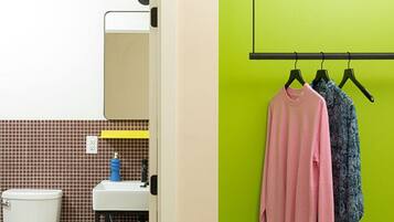 A bathroom with a white toilet, a sink, and a mirror. There is a green wall with a black rack holding two items.