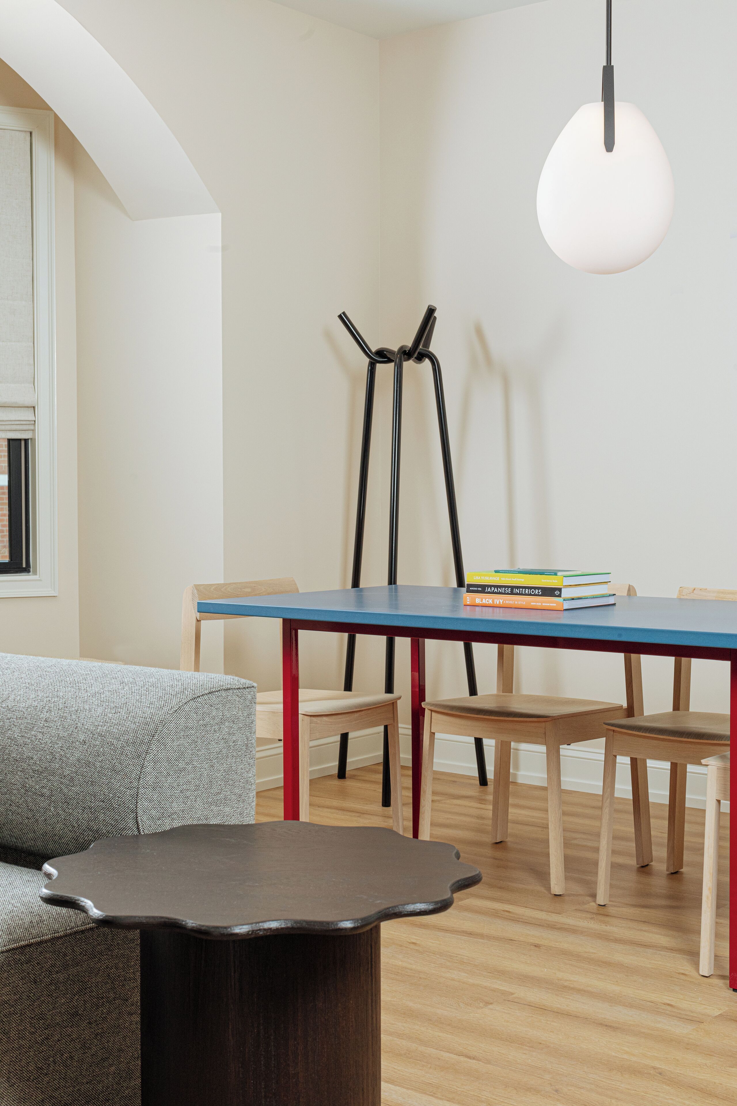 A modern dining area with a blue table, wooden chairs, a dark wooden side table, and a hanging light fixture.