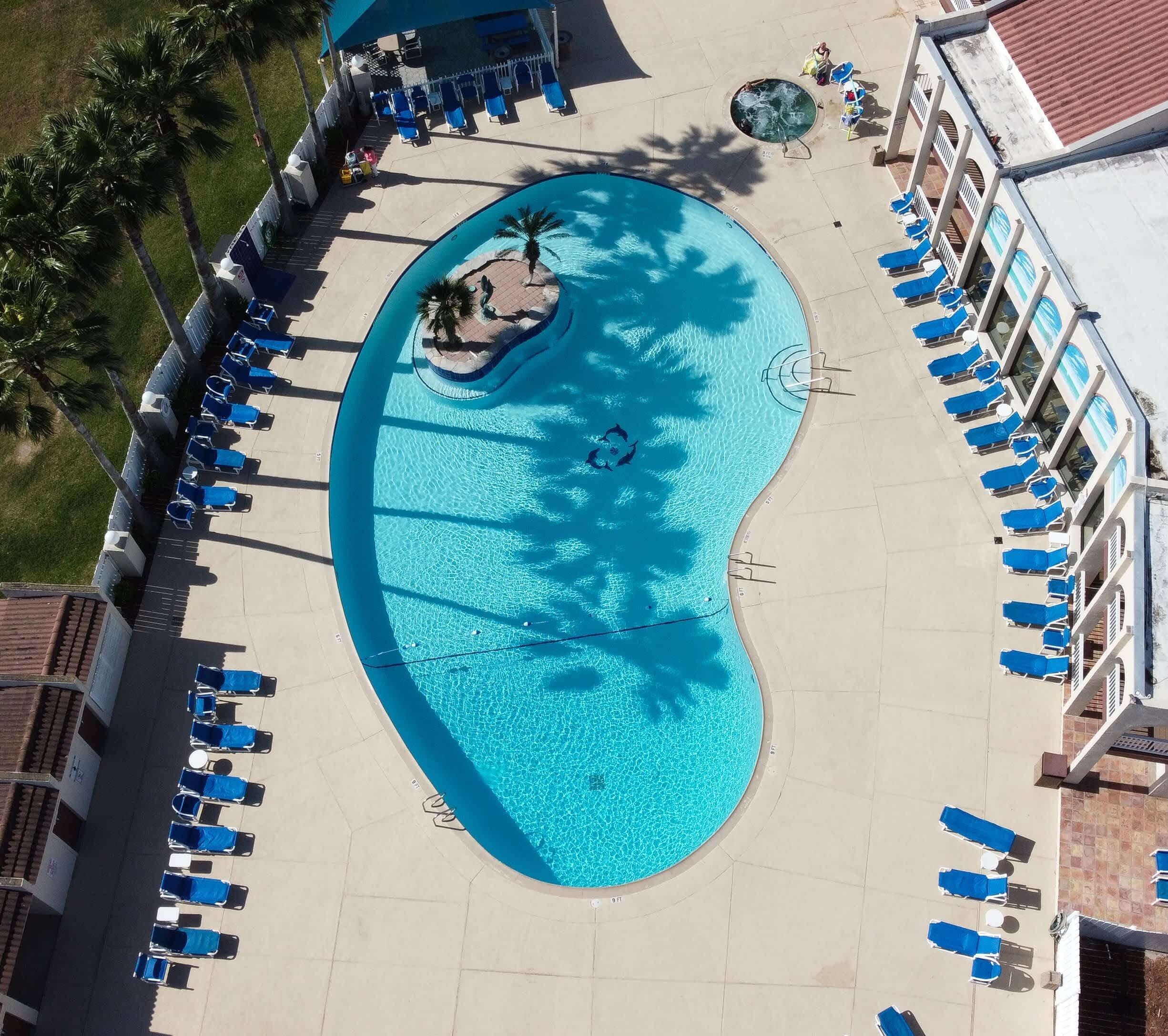 An aerial view of a swimming pool with lounge chairs and a small island, surrounded by buildings.