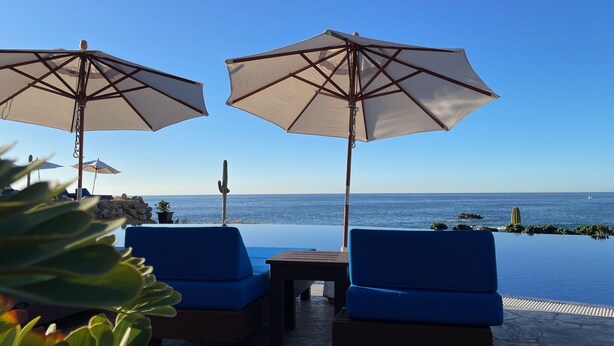 A poolside area with two blue lounge chairs and two large umbrellas, overlooking the sea.