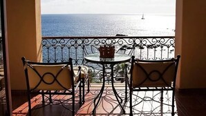A balcony with a table and two chairs, overlooking a body of water with a sailboat.