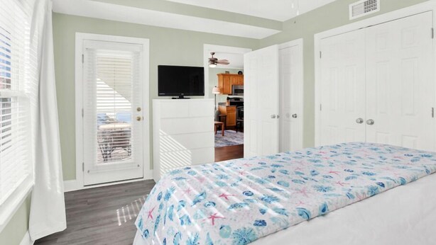 A bedroom with a bed, a TV, and a kitchenette in the background. - Great Beach Condo, Across From Heated Pool Access (Tybee Island)