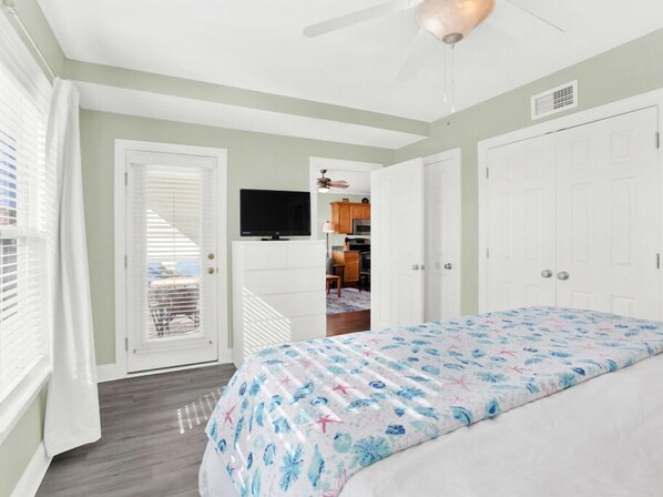 A bedroom with a bed, a TV, and a kitchenette in the background. - Great Beach Condo, Across From Heated Pool Access (Tybee Island)