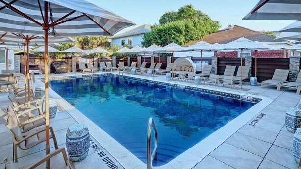 A pool area with lounge chairs and umbrellas. - Great Beach Condo, Across From Heated Pool Access (Tybee Island)