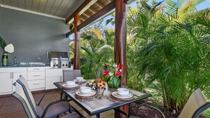An outdoor dining area with a table set for four, surrounded by chairs, and a kitchen area with a grill and sink. - 🏖️Private Lanai | Golf/Sunset Views | Pool | Keyless (Kamuela)