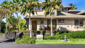 A two-story house with a tiled roof, palm trees, and a stone wall. - 🏖️Private Lanai | Golf/Sunset Views | Pool | Keyless (Kamuela)
