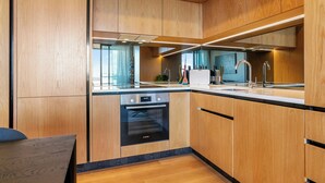 A modern kitchen with wooden cabinetry, a Bosch oven, stainless steel appliances, and a large window providing natural light.