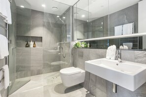 A modern bathroom with a glass-enclosed shower, a white sink, and a toilet. - Beautiful and bold 1 bed retreat (Auckland)