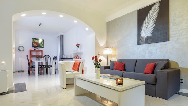 A modern living room with a grey sofa, white coffee table, and a dining area with chairs and a table.