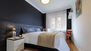 A modern bedroom with a large bed, a bedside table with a lamp, a chair, and a window with curtains.