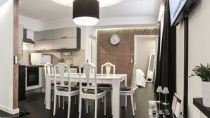 A modern kitchen with white cabinetry, a dining table with chairs, a clock on the wall, and a TV mounted on the wall.