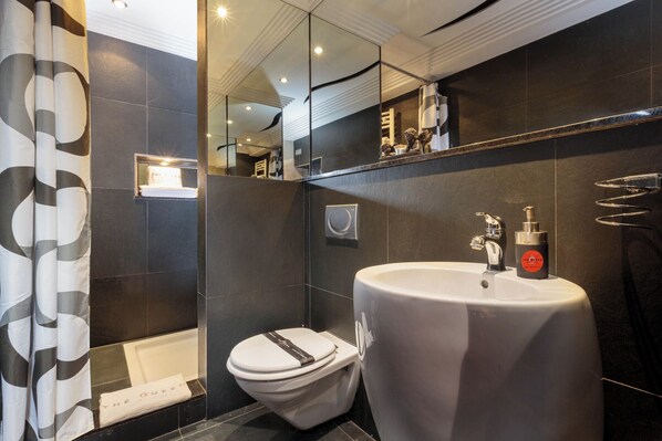 A modern bathroom with a white toilet, a large sink, and a shower area.